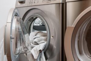 Image of a silver washing machine with the door slightly ajar and a white towel inside.