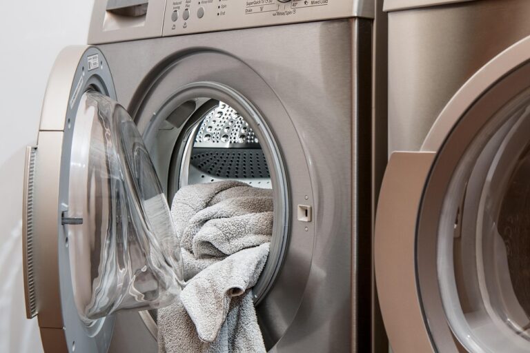 Image of a silver washing machine with the door slightly ajar and a white towel inside.