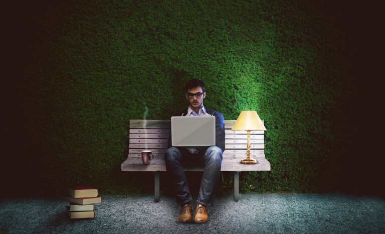 Worker on a bench with a lamp and coffee, as though they are working late into the night.