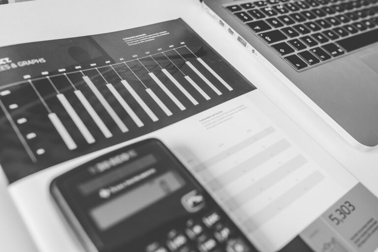 black and white image of a calculator with the edge of a laptop keyboard and a bar chart showing revenue over a period of time