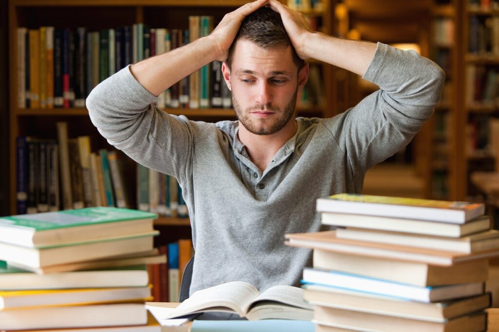 frustrated man in a gray shirt with two stacks of books and papers