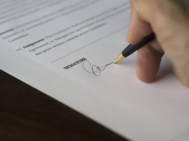 Image of a white person's hand signing a document, suggested to be for an SBA loan or due diligence.