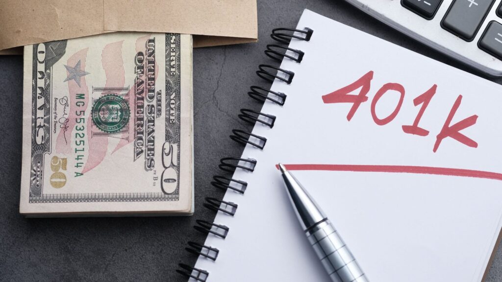 Notebook with "401k" written in red beside cash, a pen and a calculator