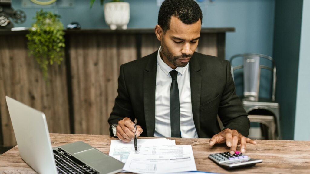 Accountant in a suit analyzing financial statements with a calculator and laptop at a desk