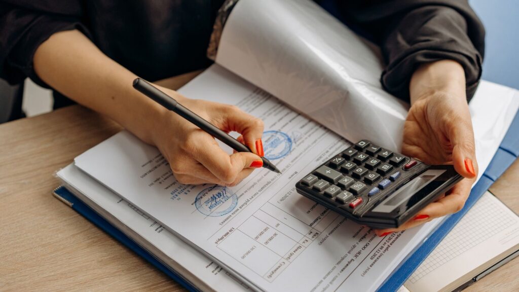 Accountant reconciling statements in a ledger binder using a calculator and pen