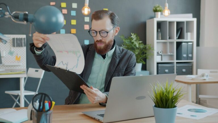 Business buyer in glasses reviewing a printed chart at his desk, representing reading a confidential information memorandum (CIM) when buying a business.