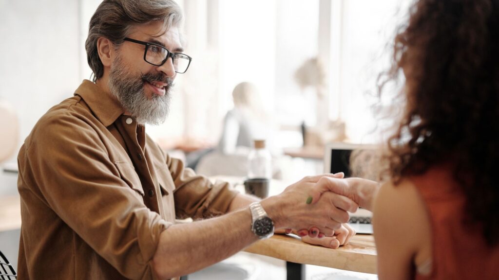 Business buyer shaking hands with a seller across a table in a bright cafe