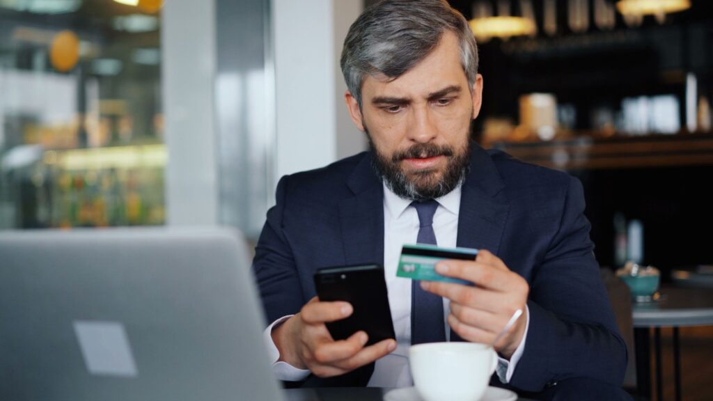 Business owner holding a bank card and smartphone while banking online at a cafe table