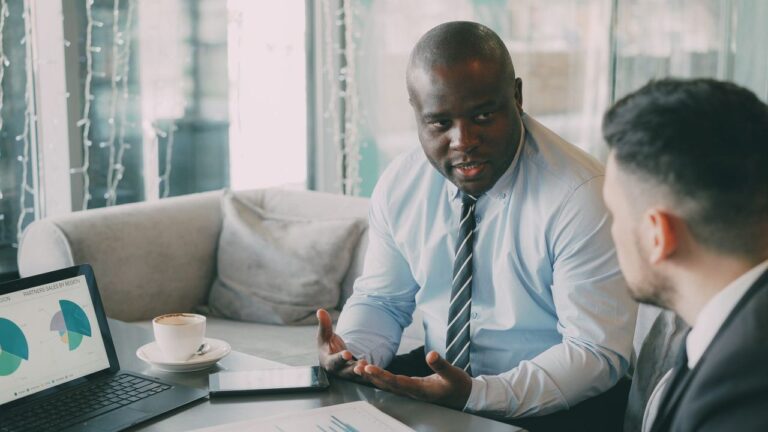 Two businessmen talking over coffee and a laptop in a café, a check-in meeting between a business owner and a client