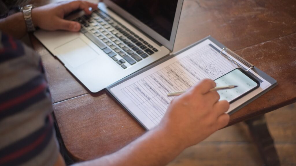 Business owner completing a filing form on a clipboard next to a laptop and smartphone