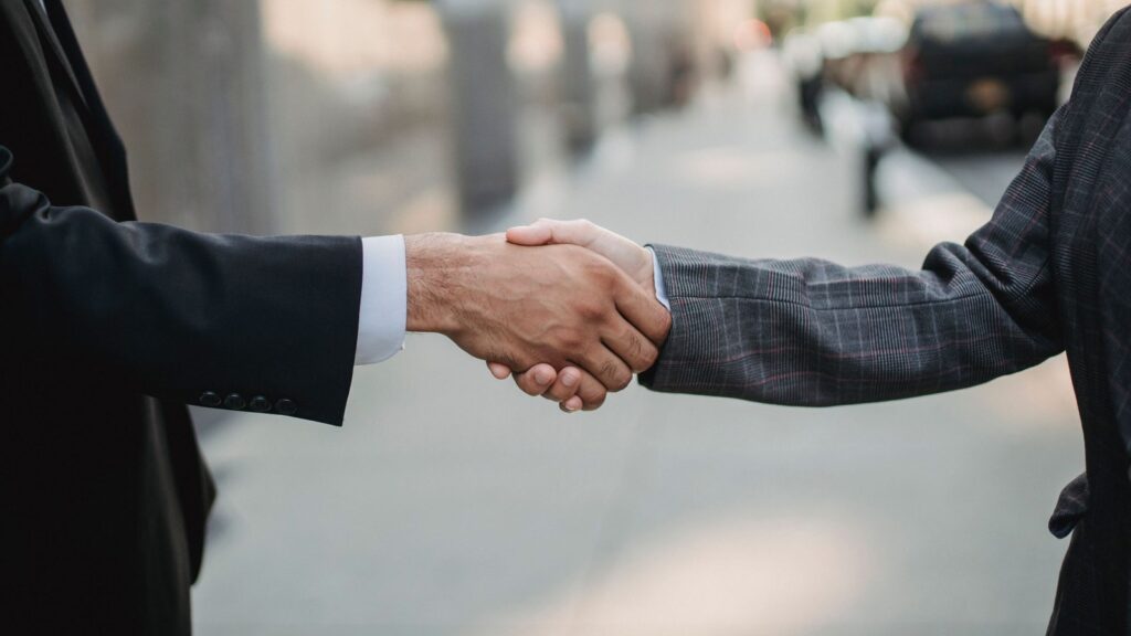 Two business professionals in suits shaking hands on a city sidewalk