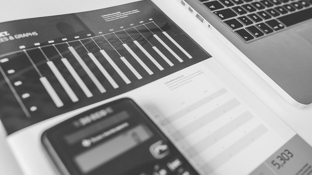Black-and-white close-up of a calculator, laptop and financial bar chart report