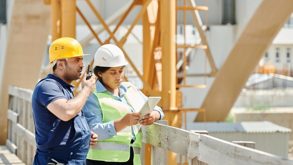 Construction project manager and engineer in hard hats reviewing a schedule on a tablet at a job site
