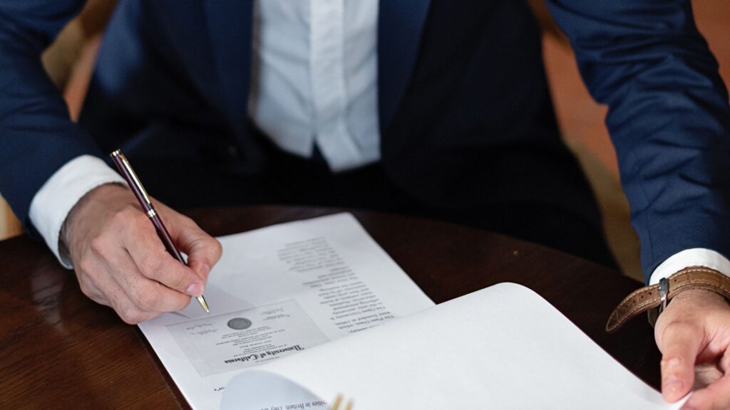 Executive in a suit signing corporate legal documents at a wooden desk