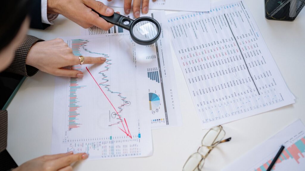 Professionals examining financial statements and charts with a magnifying glass on a white table