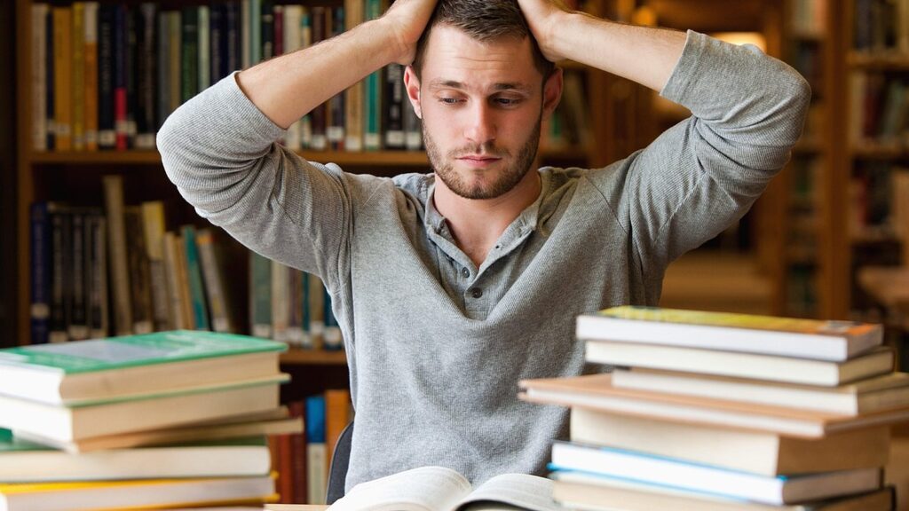 Frustrated man with his hands on his head surrounded by stacks of books in a library