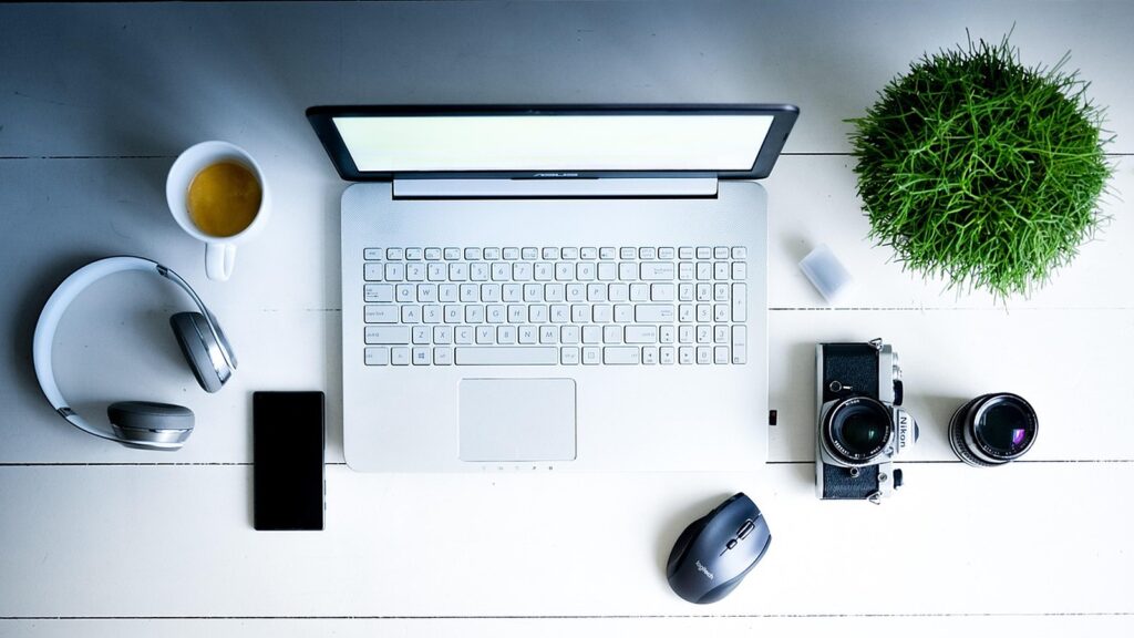 Overhead view of a tidy home office desk with a laptop, coffee, phone, camera and plant