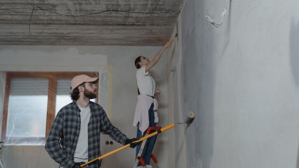 Two people renovating and painting the interior walls of a house