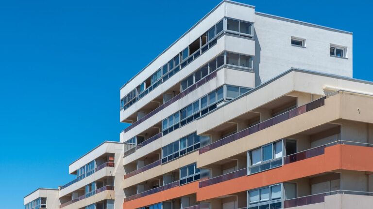 Modern multi-story apartment building with balconies against a clear blue sky