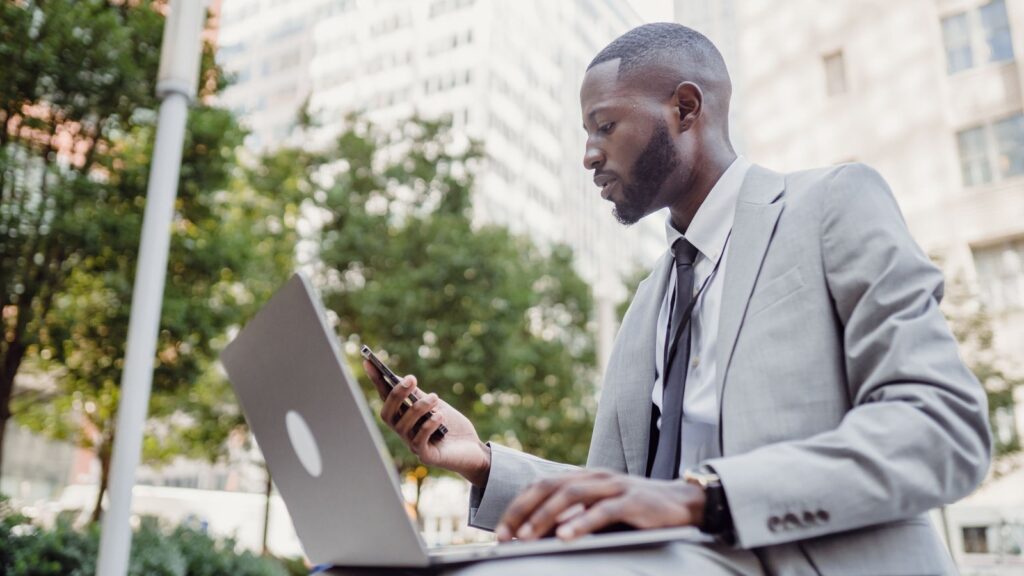 Entrepreneur in a suit working on a laptop and phone outdoors in a downtown setting