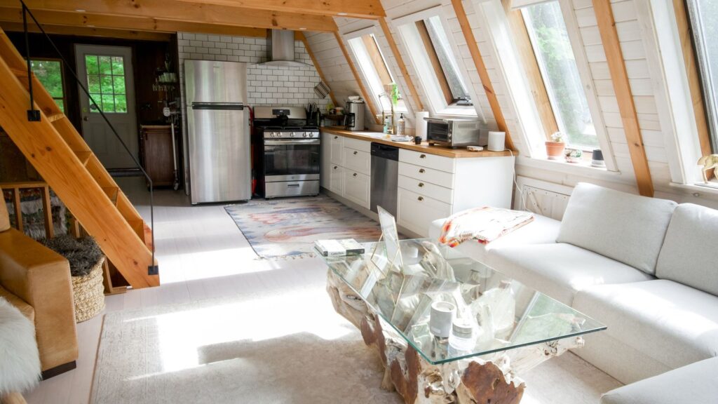 Bright A-frame cabin vacation rental interior with a white sofa, kitchen and large windows