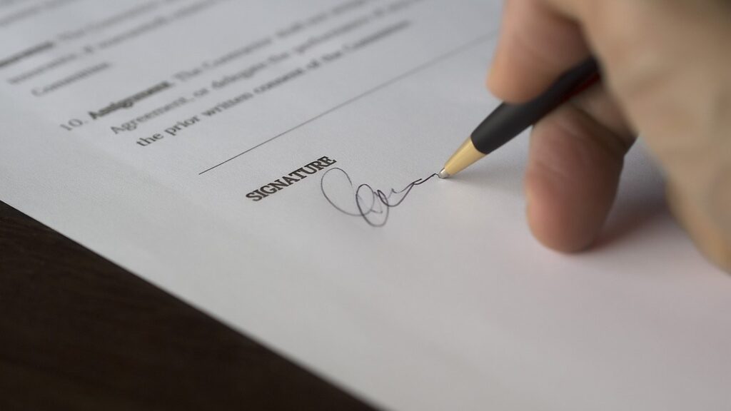 Hand signing an agreement with a pen on the signature line