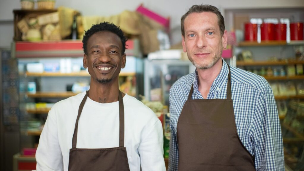Two smiling small business owners in aprons standing in their neighborhood grocery store