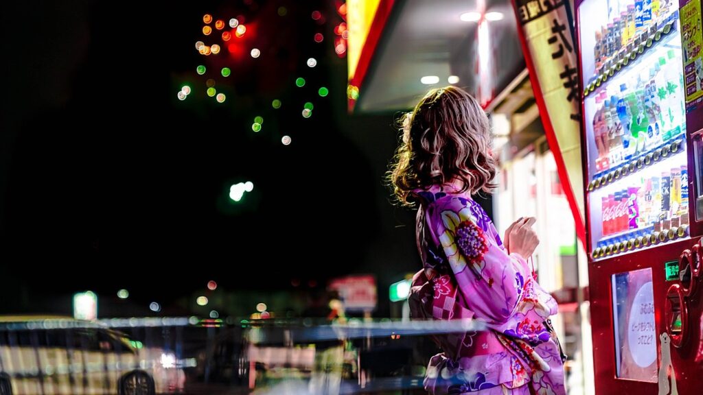 Woman standing beside lit vending machines on a street at night